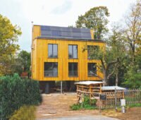 Ein Haus mit einer Holzverkleidung, oben auf dem Dach fast senkrecht installiert eine Solarthermie-Anlage.