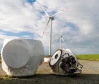 Repowering: Im Vordergrund eine alte verrostete Nabe der abgebauten Anlage und die größere der neuen Turbine. Im Hintergrund: mehrere Windenergieanlagen.