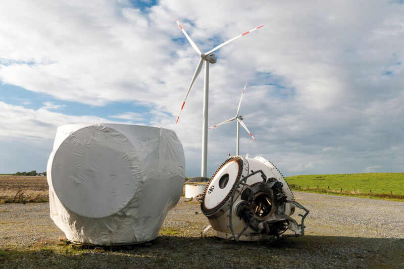 Repowering: Im Vordergrund eine alte verrostete Nabe der abgebauten Anlage und die größere der neuen Turbine. Im Hintergrund: mehrere Windenergieanlagen.