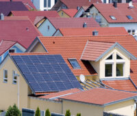 Viele Dächer von Ein- und Zweifamilienhäusern, davon im Vordergrund ein Dach mit einer blauen Photovoltaikanlage