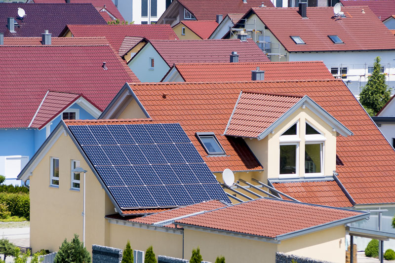 Viele Dächer von Ein- und Zweifamilienhäusern, davon im Vordergrund ein Dach mit einer blauen Photovoltaikanlage