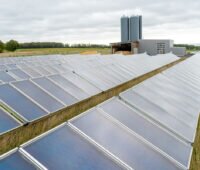 Kollektorreihen der Solarthermieanlage in Mengsberg. Im Hintergrund: das Heizhaus mit zwei Wärmespeichern.