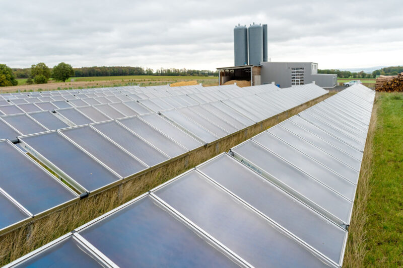 Kollektorreihen der Solarthermieanlage in Mengsberg. Im Hintergrund: das Heizhaus mit zwei Wärmespeichern.