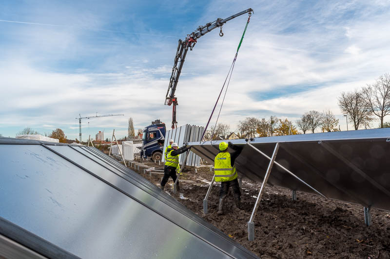 Solarthermie: Bauarbeiter bugsieren einen Großkollektor, der an einem Kran hängt, in seine Halterung