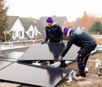 Zwei Monteure installieren große PV-Module auf einem Flachdach.