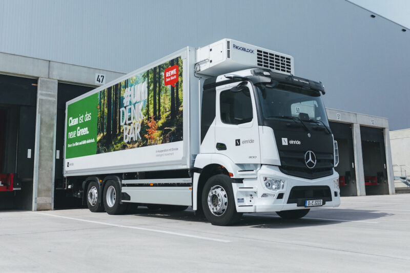 Ein weißer E-LKW von schräg vorn gezeigt mit Aufschrift aus weißer Schrift auf Apfelgrün: Dieser LKW fährt und kühlt elektrisch.