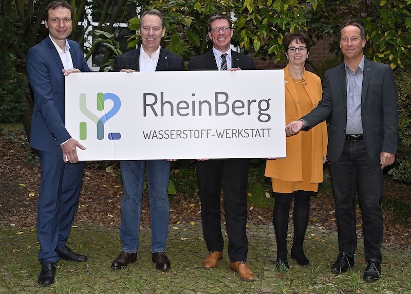 Vier Männer und eine Frau halten ein Schild, auf dem "Wasserstoff-Werkstatt RheinBerg" steht.