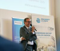 Redner mit Mikro auf der Konferenzbühne aus Perspektive des Publikums