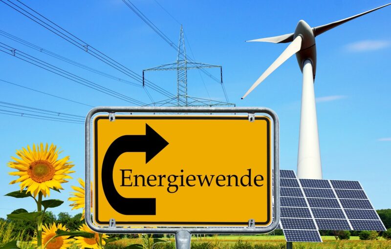 Ein animiertes Bild zeigt ein Verkehrsschild, das auf die Energiewende zeigt udn im Hintergrund Wind, Solarenergie udn Strommasten.