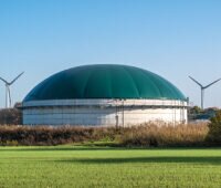 Biogasanlage im Vordergrund, rechts und links Windkraftanlagen.