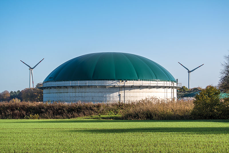 Biogasanlage im Vordergrund, rechts und links Windkraftanlagen.