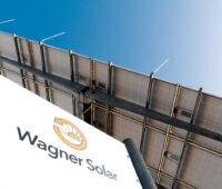 Wagner-Solar-Schild unten links, darüber vor blauem Himmel die Rückseite einer Photvoltaikanlage