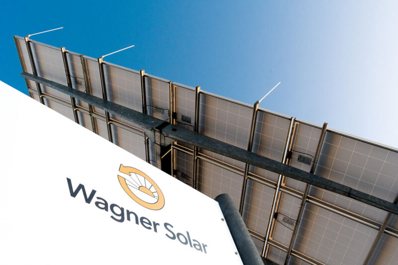 Wagner-Solar-Schild unten links, darüber vor blauem Himmel die Rückseite einer Photvoltaikanlage