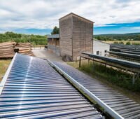 Holzheizwerk im Hintergrund, im Vordergrund: Solarthermieanlage. Symbolbild für sparsame Bioenergienutzung laut Biomassestrategie