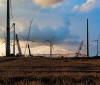 Kräne und bereits aufgestellte Windkraftmasten ragen in den Himmel: eine Baustelle für den Aufbau eines neuen Windparks