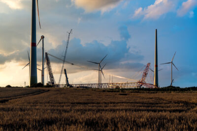 Kräne und bereits aufgestellte Windkraftmasten ragen in den Himmel: eine Baustelle für den Aufbau eines neuen Windparks