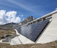Zu sehen ist eine PV-Anlage an einer Staumauer vor einem Bergpanorama.