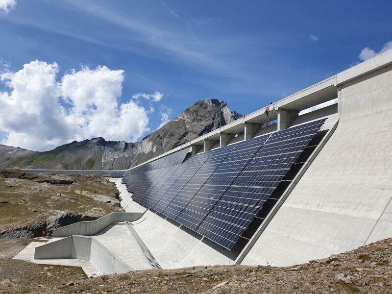 Zu sehen ist eine PV-Anlage an einer Staumauer vor einem Bergpanorama.