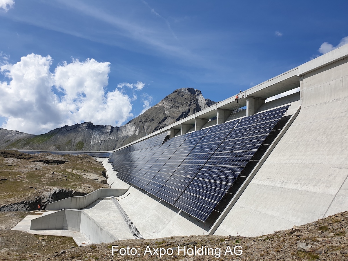 Zu sehen ist eine PV-Anlage an einer Staumauer vor einem Bergpanorama.