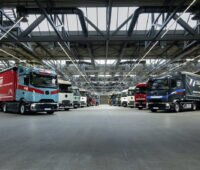 14 Trucks sind in einer riesigen Halle in zwei Reihen gegenüber stehend aufgereiht. Sie sind schräg nach vorn nebeneinander ausgerichtet.