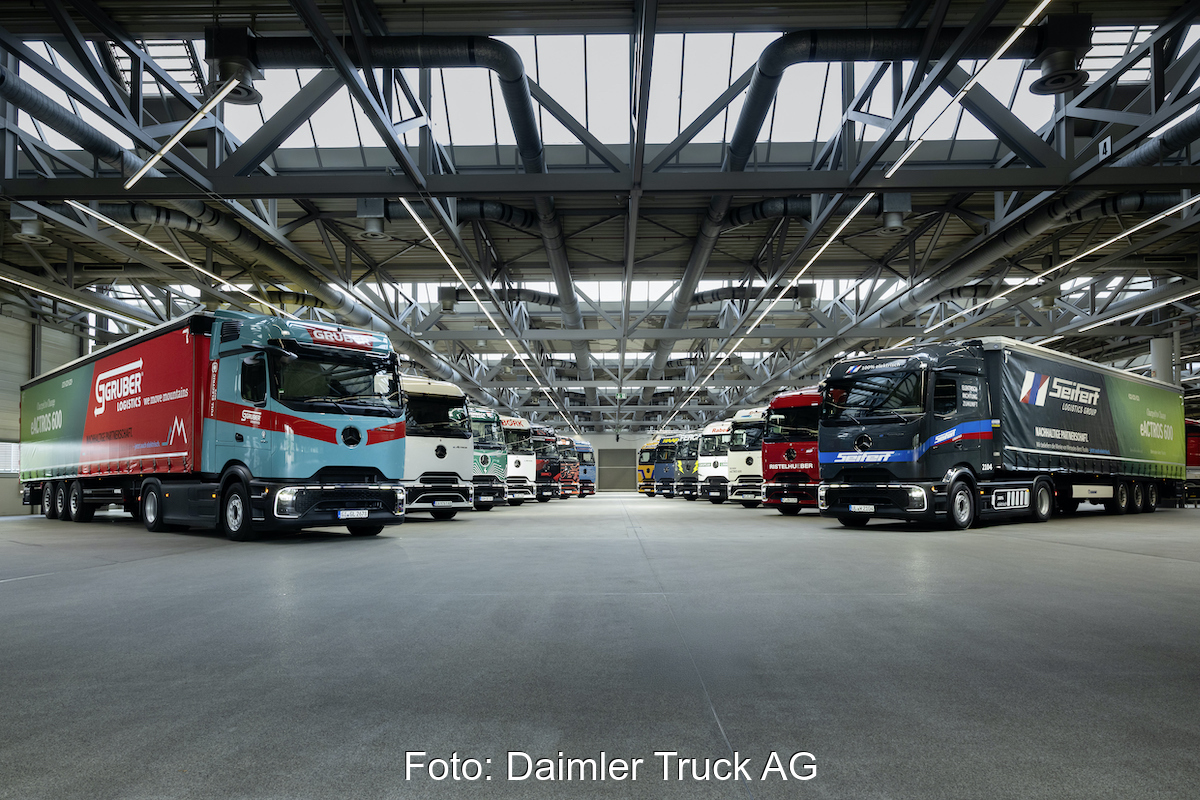 14 Trucks sind in einer riesigen Halle in zwei Reihen gegenüber stehend aufgereiht. Sie sind schräg nach vorn nebeneinander ausgerichtet.