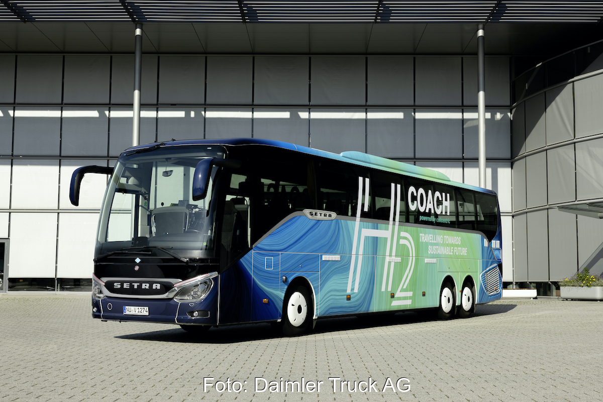 Ein Omnibus ist auf einem Betriebsgelände von schräg recht nach vorn aufgenommen. Er trägt auf blau bis türkisfarbenen Meeresfarben den Schriftzug H₂ Coach.