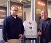 Sohn und Vater stehen nebeneinander und halten zum Firmenjubiläum "40 Jahre EWS" ein Glas mit Flüssigkeit in der Hand.