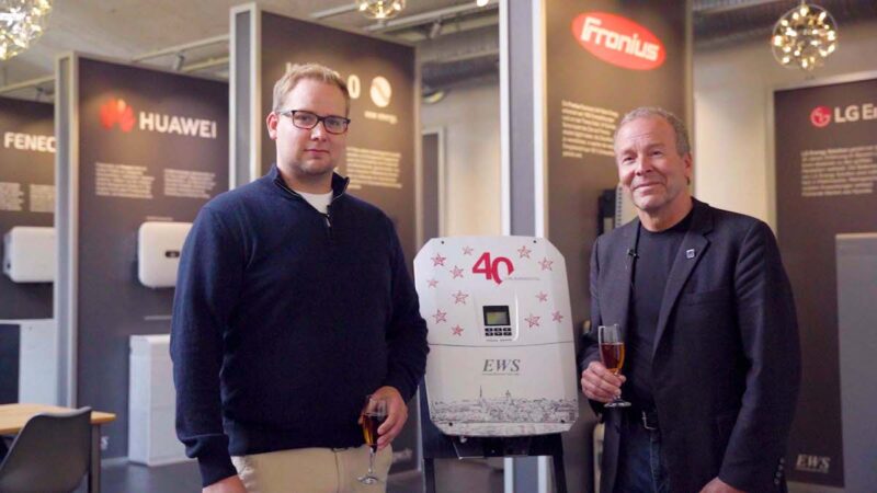 Sohn und Vater stehen nebeneinander und halten zum Firmenjubiläum "40 Jahre EWS" ein Glas mit Flüssigkeit in der Hand.