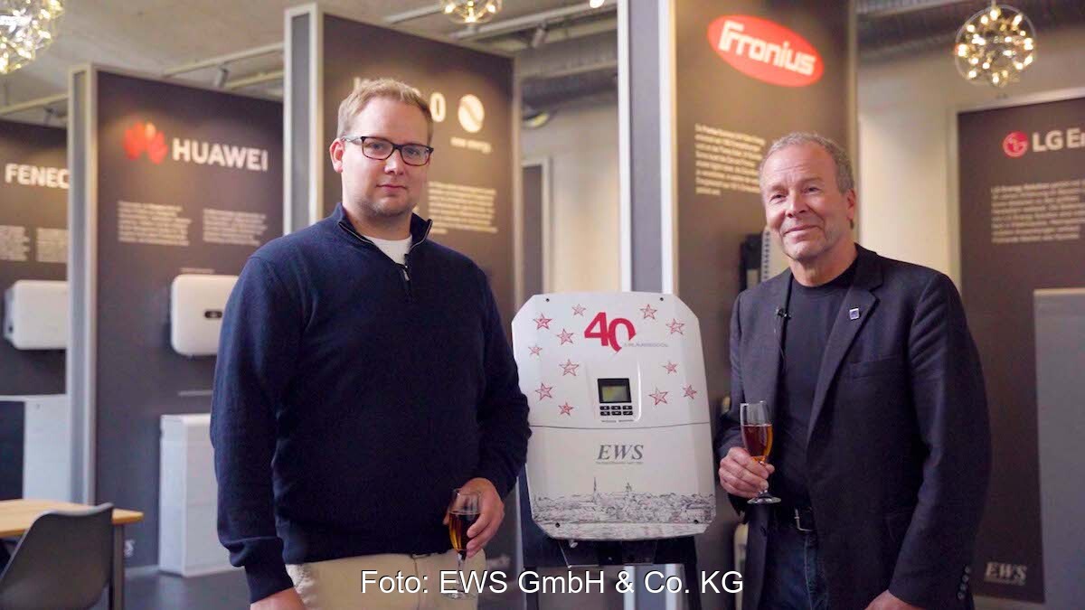Sohn und Vater stehen nebeneinander und halten zum Firmenjubiläum "40 Jahre EWS" ein Glas mit Flüssigkeit in der Hand.