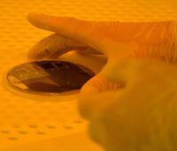 Eine Hand mit einer Solarzelle im Labor in orangefarbenem Licht - die Weltrekord-Solarzelle des Fraunhofer ISE.