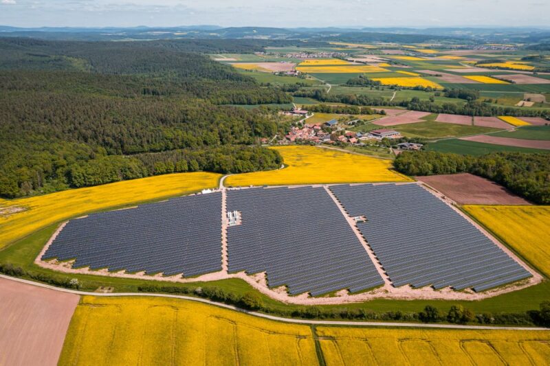 Luftaufnahme einer Freiflächen-PV-Anlage umgeben von gelben Feldern.