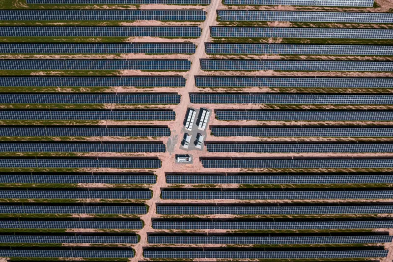 Ein Hybridkraftwerk aus Photovoltaik und Windenergie auf grüner Wiese unter blauem Himmel.