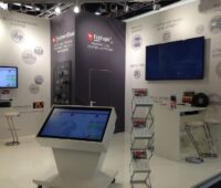 Ein Messestand mit Bildschirmen, Prospekten und Aufstellern zu IT-Produkten der Firma AIS Automation
