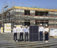 Sechs Personen un ein großes Solarmodul auf einer Baustelle.