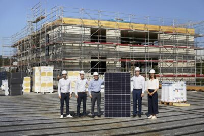 Sechs Personen un ein großes Solarmodul auf einer Baustelle.