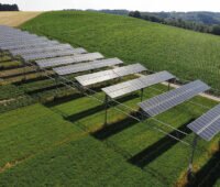 Auf einen hügelig ansteigenden Feld ist eine aufgeständerte PV-Anlage zu sehen.