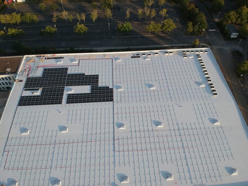 Zu sehen ist ein Luftbild einer beginnenden PV-Montage von Adler Smart Solutions auf einem großen Flachdach.