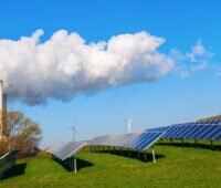 Rechts und im Vordergrund Photovoltaik-Module auf einer grünen Wiese, im Hintergrund Windkraftanlagen, links ein fossiles Kraftwerk - Energiewende ist Wahlkampf-Thema