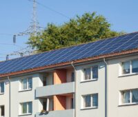 Ein Mehrfamilienhaus-Block mit großflächiger Photovoltaik-Anlage auf dem Dach.