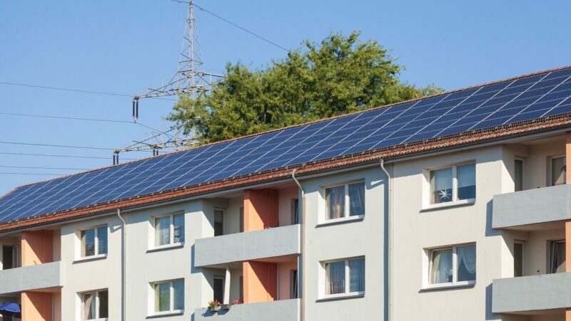 Ein Mehrfamilienhaus-Block mit großflächiger Photovoltaik-Anlage auf dem Dach.