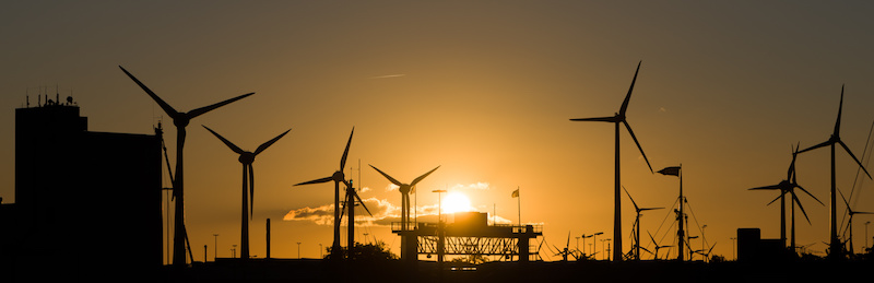 Bei untergehender Sonne Windkraftanlagen mit Industrieanlagen