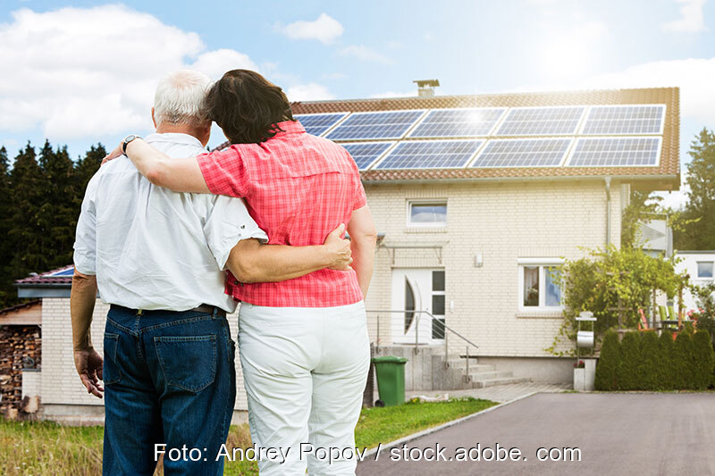 Vorn ein älteres Paar, im Hintergrund ein Einfamilienhaus mit einer Photovoltaik-Anlage auf dem Dach