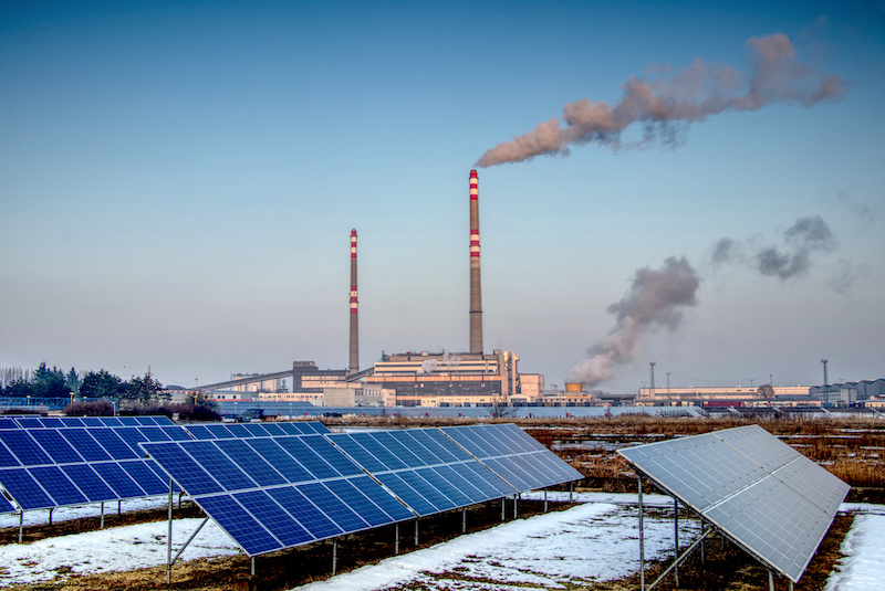 Photovoltaikanlage vor Kohlekraftwerk mit rauchenden Schloten