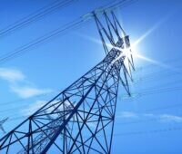 Strommasten im Sonnenlicht, erstmals liefert Photovoltaik in Deutschland Sekundärregelleistung zur Stabilisierung des Stromnetzes.