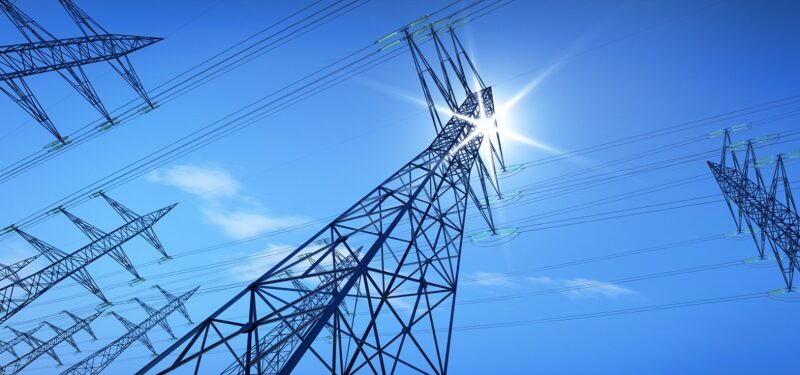 Strommasten im Sonnenlicht, erstmals liefert Photovoltaik in Deutschland Sekundärregelleistung zur Stabilisierung des Stromnetzes.