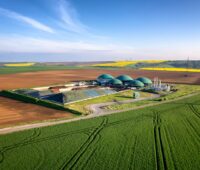 In einer Feldlandschaft steht eine Biogasanlage. Bei Aufbereitung von Biogas zu Biomethan, kann es auch in Gasheizungen zum Einsatz kommen.