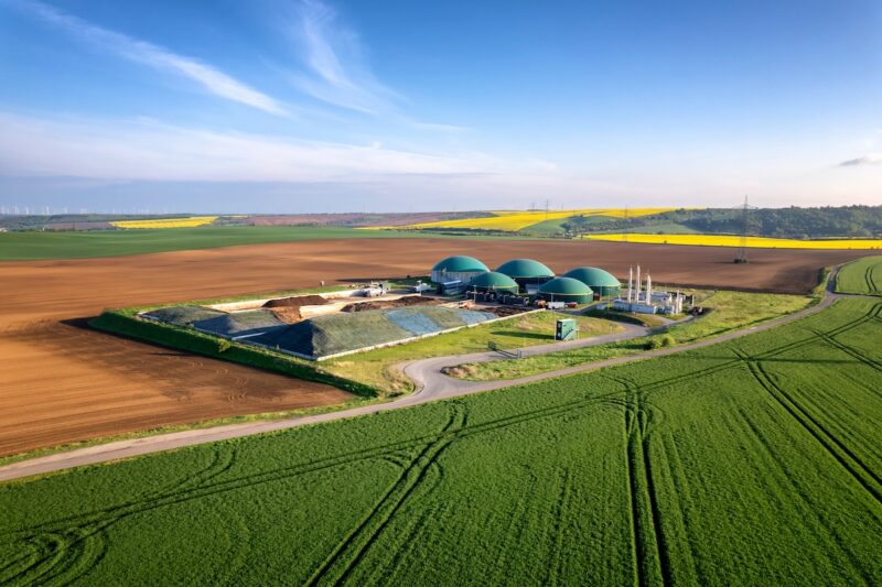 In einer Feldlandschaft steht eine Biogasanlage. Bei Aufbereitung von Biogas zu Biomethan, kann es auch in Gasheizungen zum Einsatz kommen.
