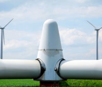 Rotorkopf einer Windkraftanlage abgebaut auf dem Rasen liegend, im Hintergrund zwei Windkraftanlagen in Betrieb