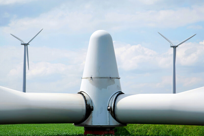 Rotorkopf einer Windkraftanlage abgebaut auf dem Rasen liegend, im Hintergrund zwei Windkraftanlagen in Betrieb