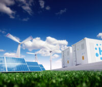 Auf einer grünen Wiese stehen links Solarmodule, im Hintergrund Windkraftanlagen, rechts Container mit der Aufschrift H2 - Hydrogen (Wasserstoff)